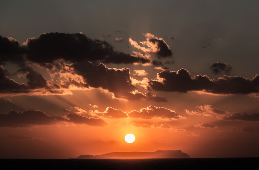 The sun set over a Greek islet at Crete's shore.